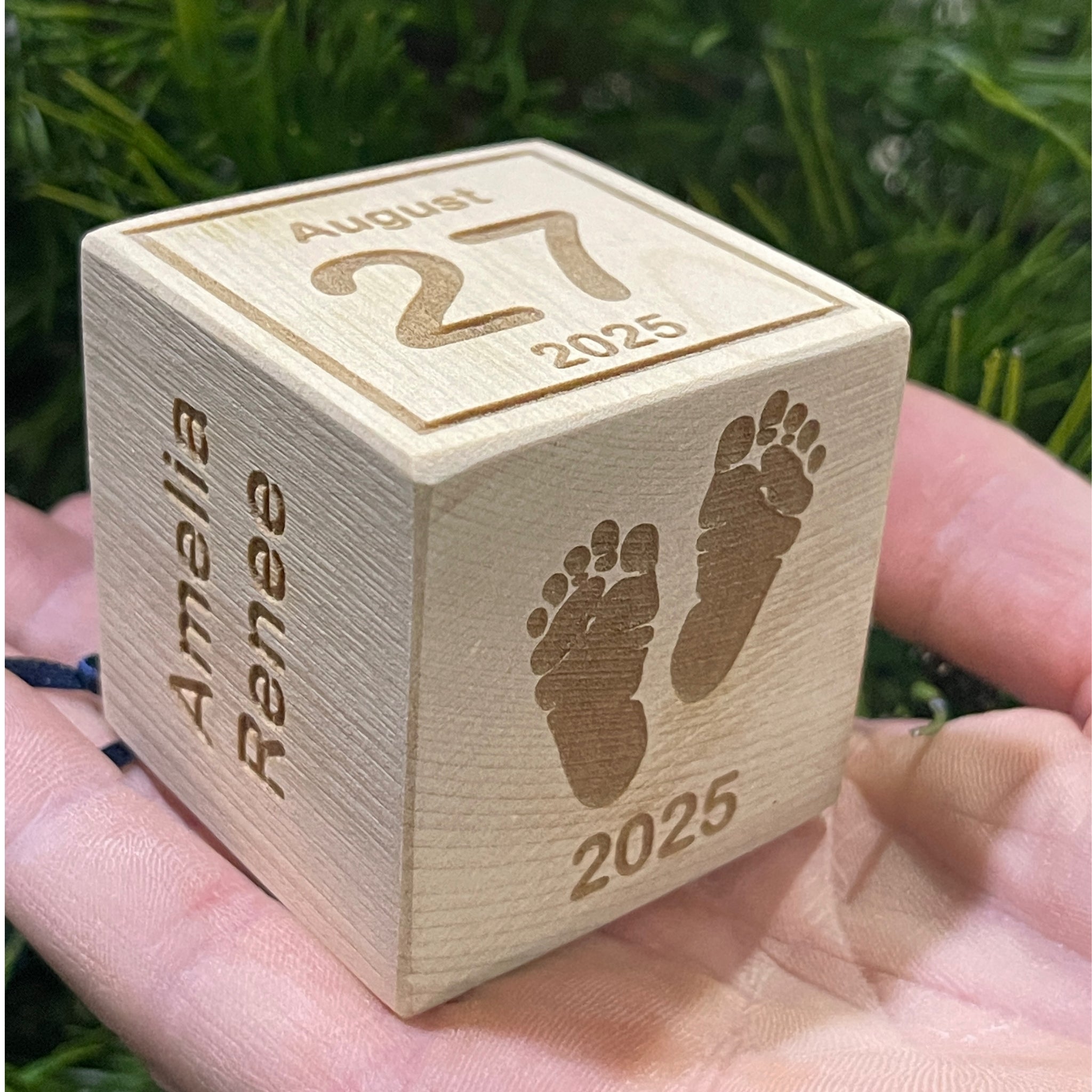 Wooden baby block ornament held in hand showing engraved baby footprints and year