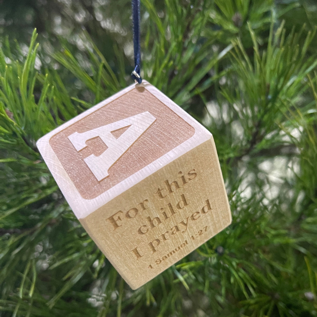Laser-engraved wooden baby block Christmas ornament hanging on a tree branch