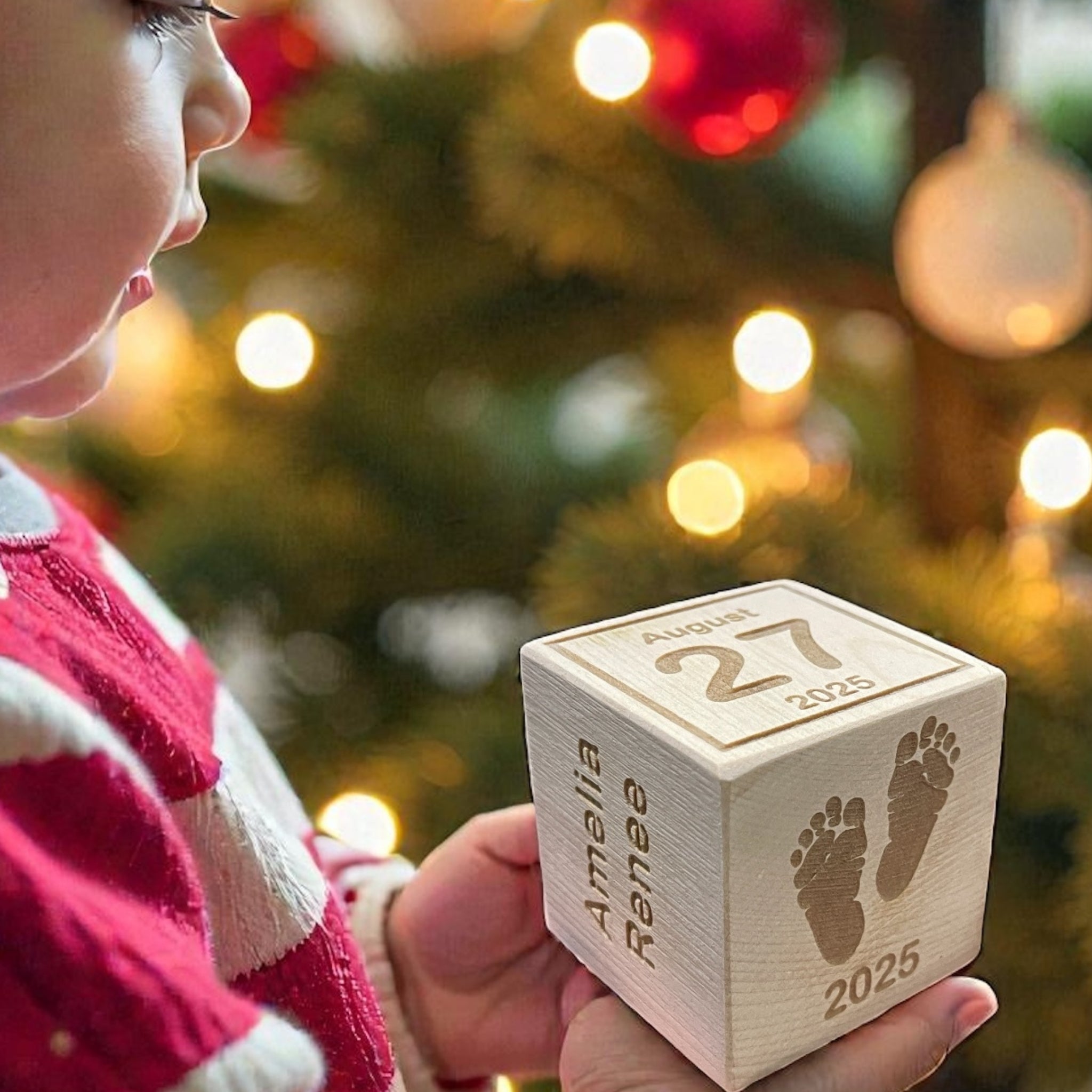 Child holding a wooden Ornament block with engraved date and name in front of a Christmas tree.