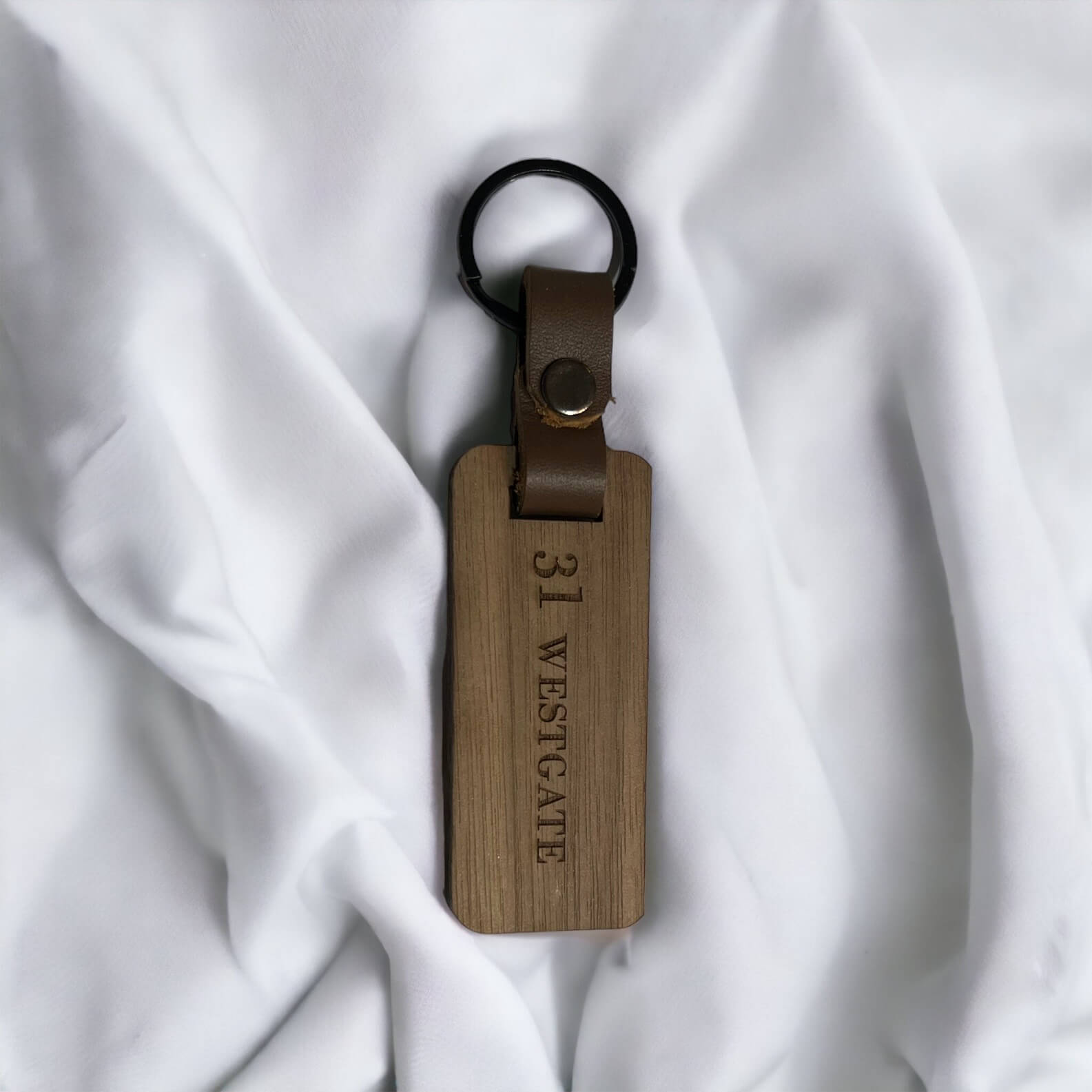 photo of one walnut hardwood keychain on a white fabric background. 