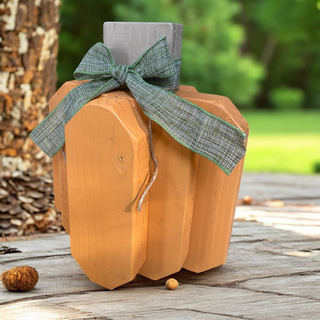 Wooden pumpkin with a green ribbon on a wooden surface outdoors