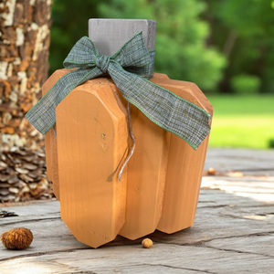 Wooden pumpkin with a green ribbon on a wooden surface outdoors