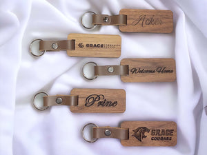 Image showing 5 handmade laser engraved walnut keyrings on a white fabric background. See more at SawyerCustomCrafts.Com