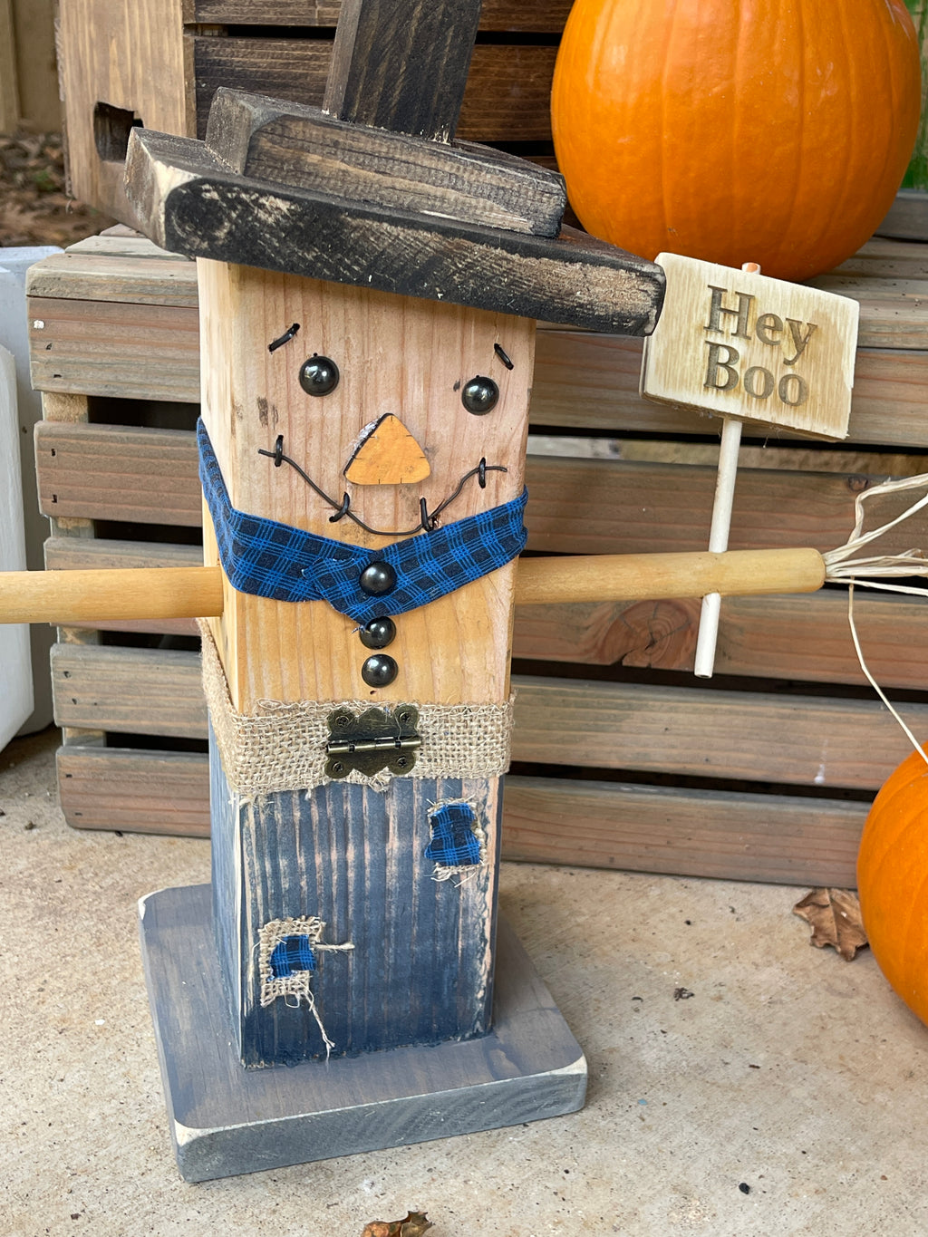 Finished wooden scarecrow with a sign that says "hey boo" on it

