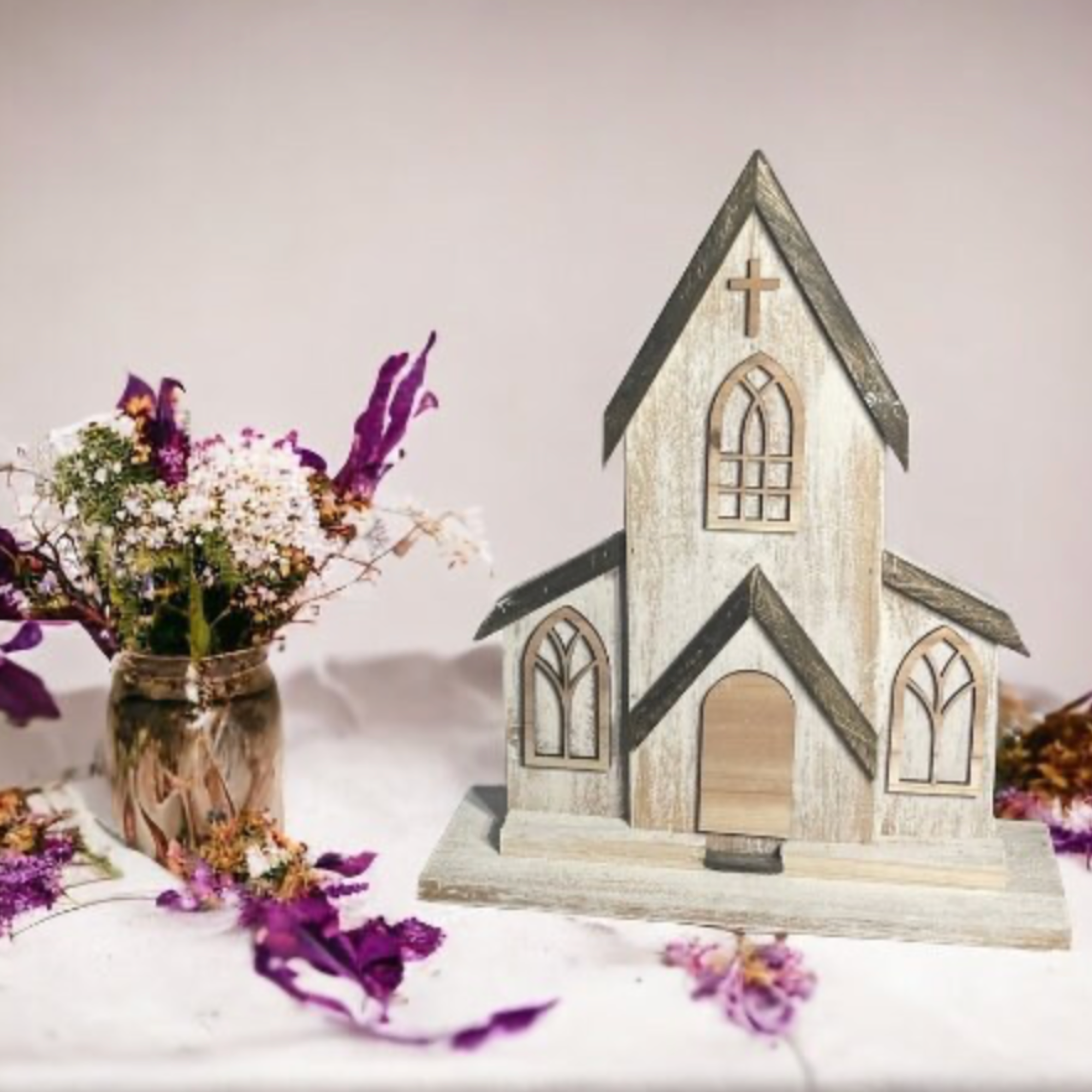 two-piece handcrafted cedar church on a tabletop surrounded by dried floral arrangements. Distressed white paint finish adds vintage farmhouse appeal. Ideal for church decorations, wedding centerpieces, or seasonal home displays.