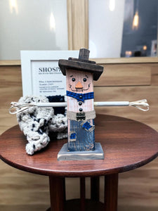Close-up view of a handcrafted wooden scarecrow showing hand-painted face details, fabric scarf, and distressed wood texture.
