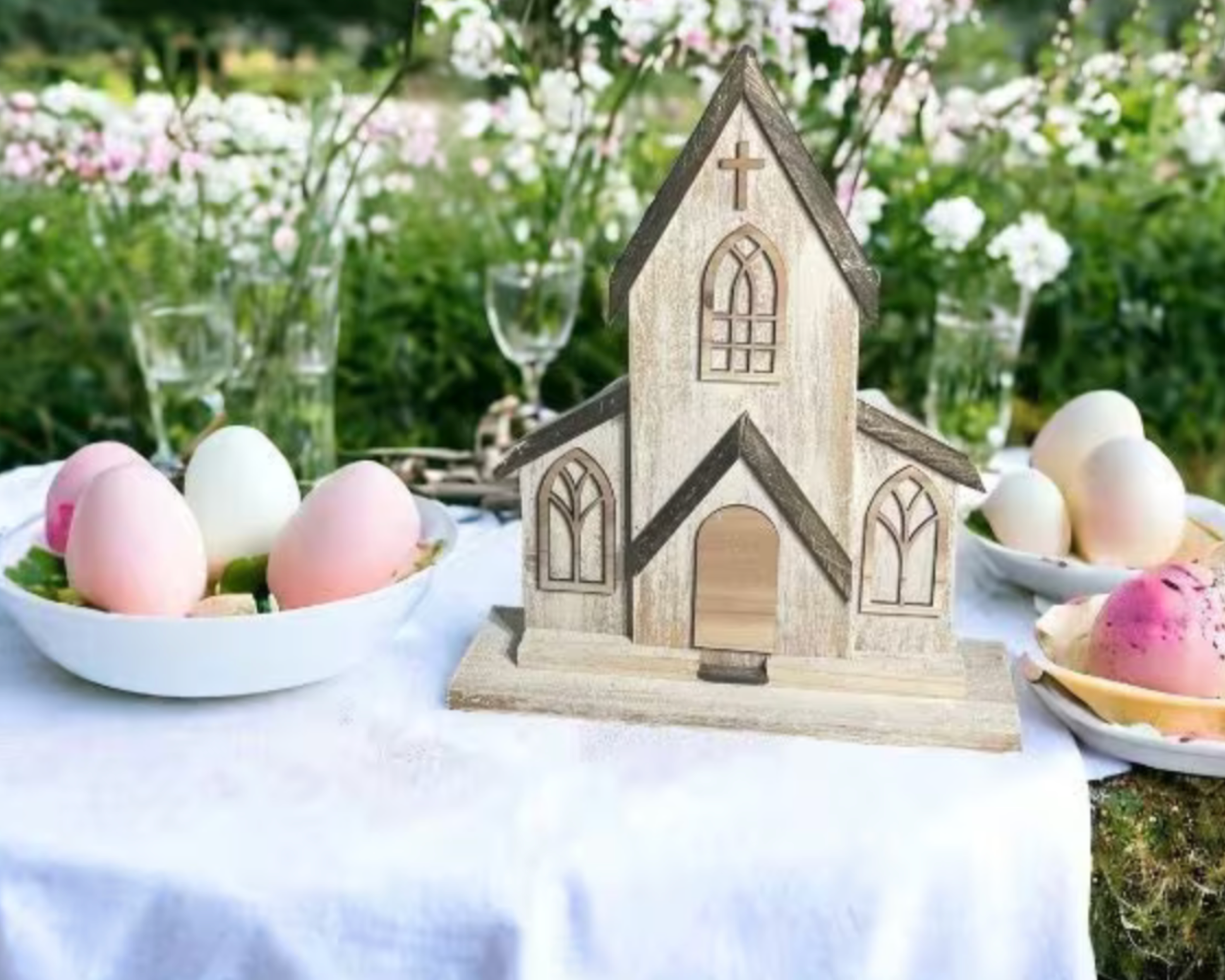 Handmade two-piece wooden church decor displayed outdoors on a white tablecloth with spring flowers and pastel Easter eggs. Distressed white cedar finish and natural wood roof give it a rustic farmhouse charm, ideal for Christian home decor, Easter displays, or wedding centerpieces.