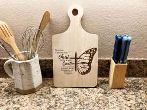 Decorate with Scripture this season with this Bible themed cutting board. Shown here on a countertop with some decorations digging to the left and the right of it. 