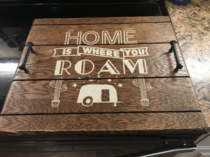 Picture of RV sized Stove Top Cover. This Cover is stained in Espresso Stain with the words "Home is where you Roam" painted on in cream colored paint. Also has a small picture of an RV With a picture of a cactus on either side of it. Find more info at SawyerCustomCrafts.com